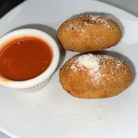 Two golden-brown fried food items sprinkled with cheese, next to a small bowl of red sauce.