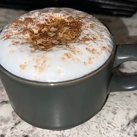 Close-up of a gray mug filled with a frothy coffee drink, sprinkled with spices on top.