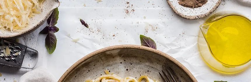 Overhead shot of pasta with ingredients such as basil, olive oil, and cheese grater.