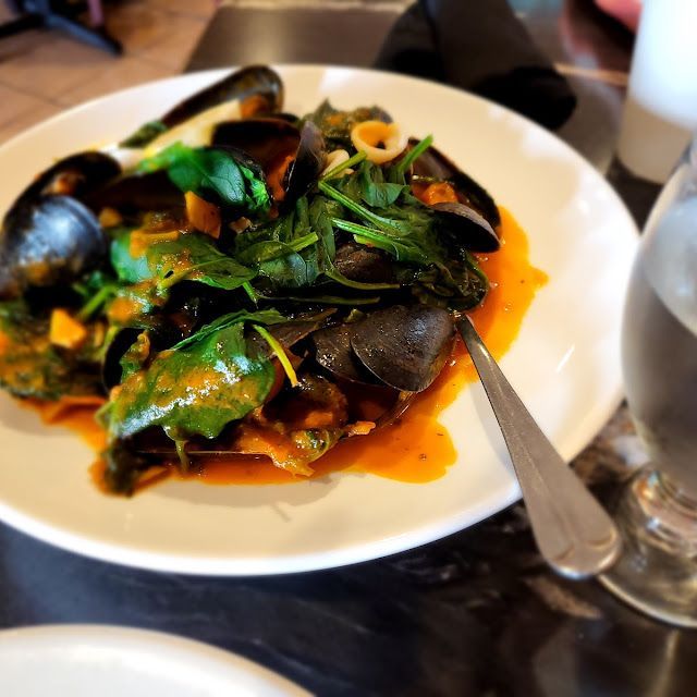 Mussels in orange sauce with spinach on a white plate, restaurant table.