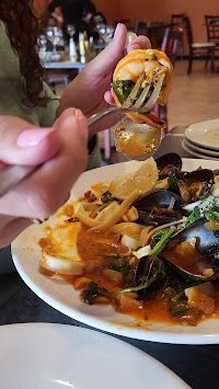 Person eating seafood dish with spoon; includes mussels, shrimp, and sauce.