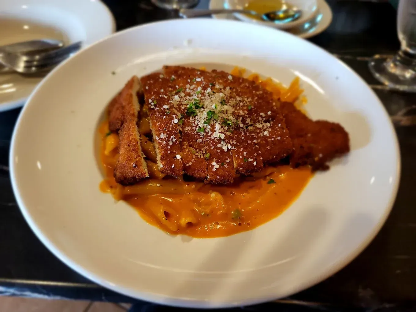 Breaded chicken cutlet with orange sauce, grated cheese, and parsley on a white plate.