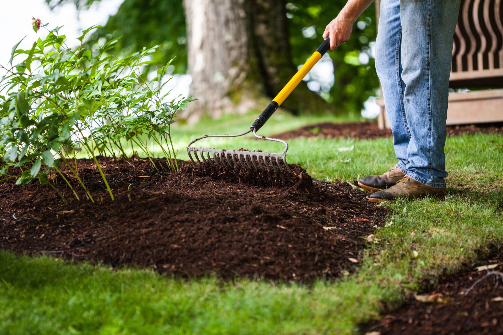 Man with garden rake standing above a pile of garden mulch.