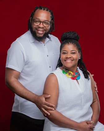 A man and a woman are posing for a picture in front of a red background.