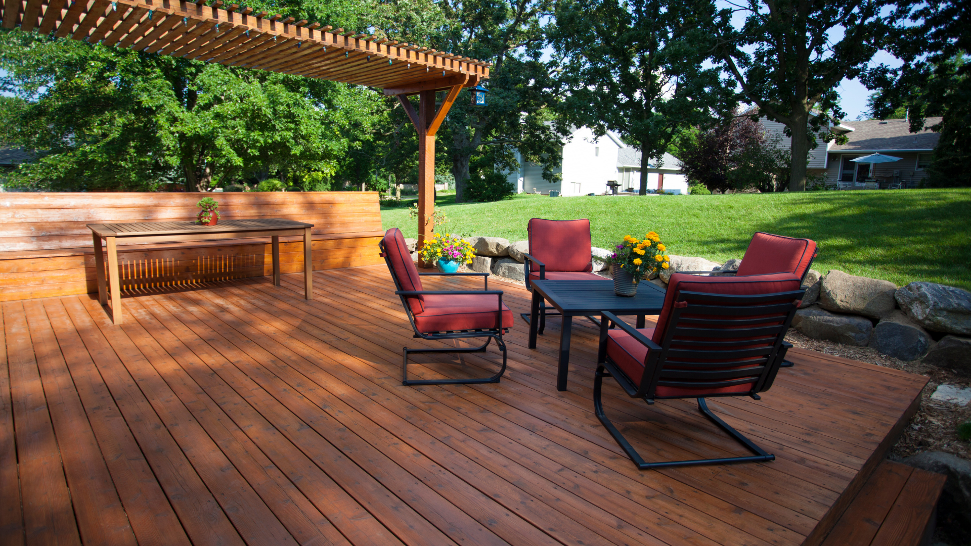 Wooden deck with outdoor seating area in a backyard, under a pergola.