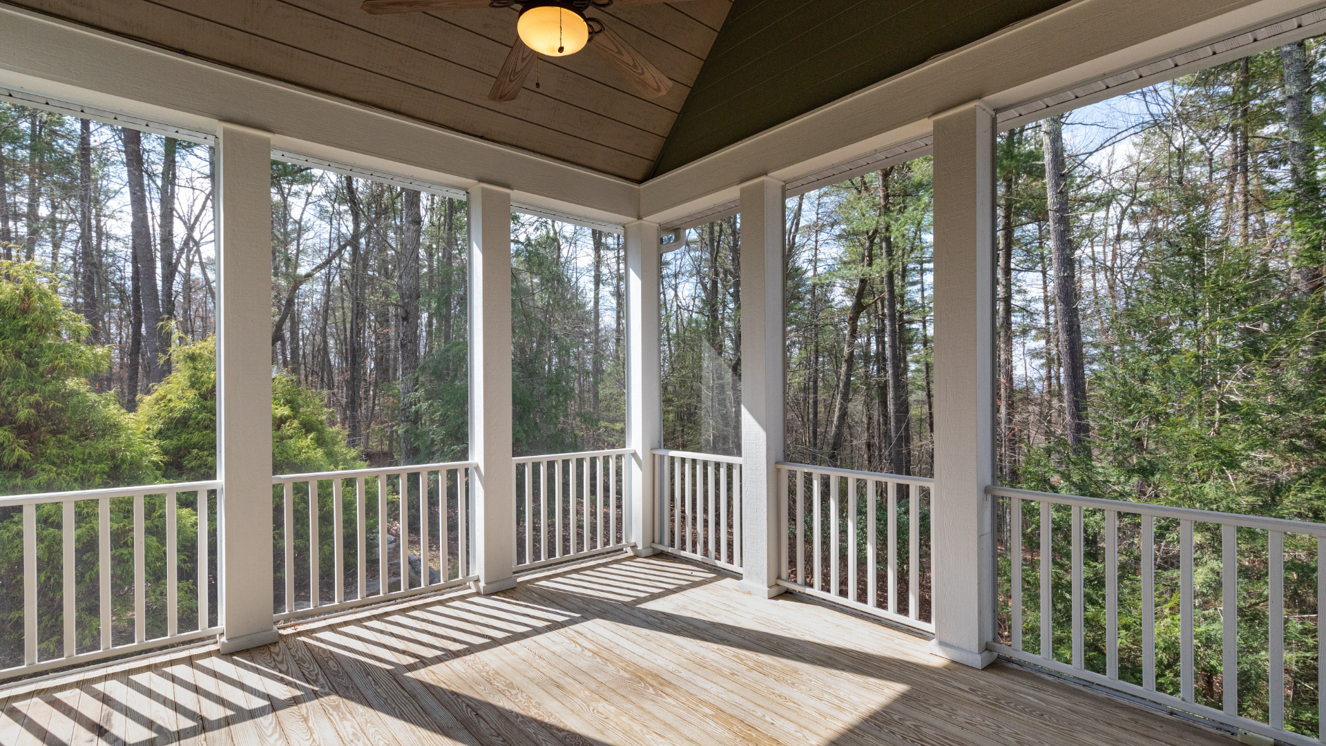 Covered porch with white railings and columns, overlooking a forest.