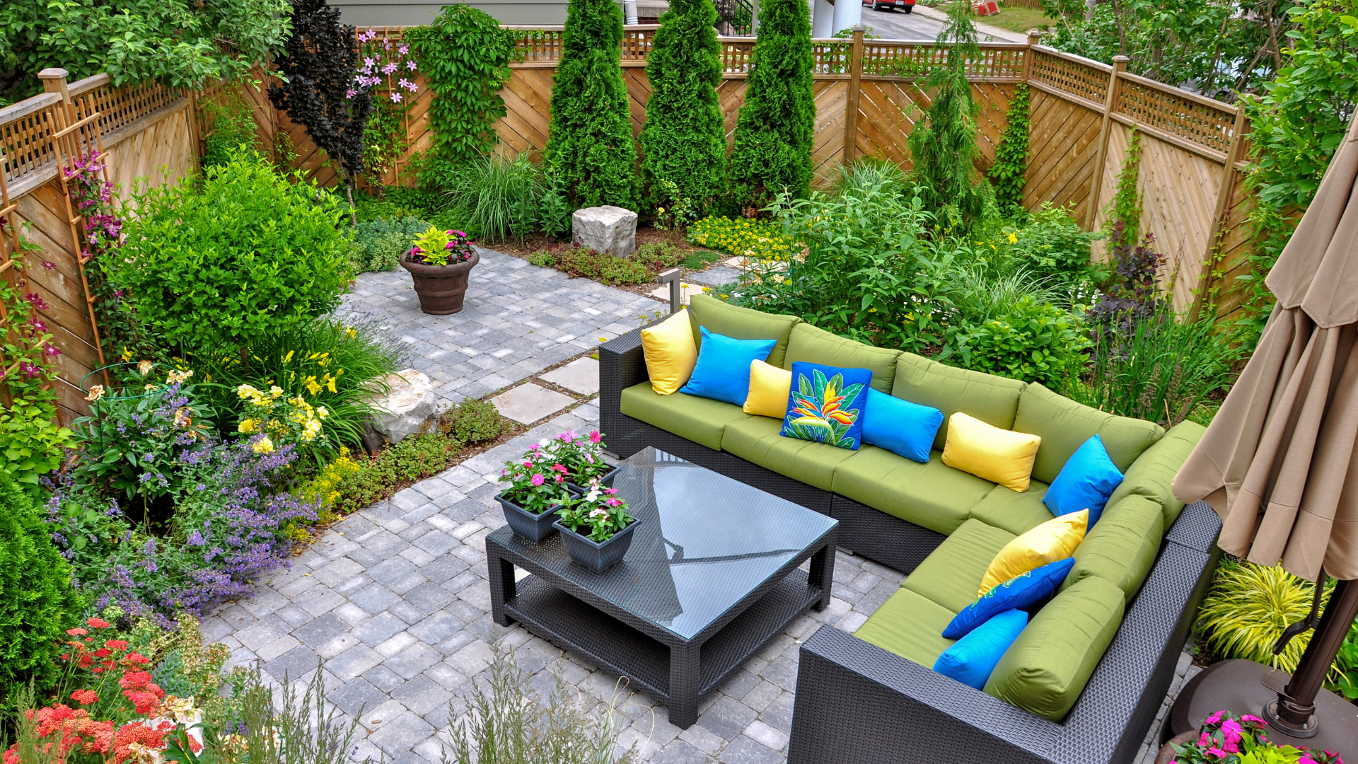 A patio with a couch , table and umbrella in a garden.
