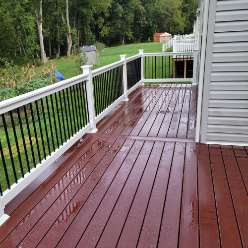 A wooden deck with a white railing and trees in the background