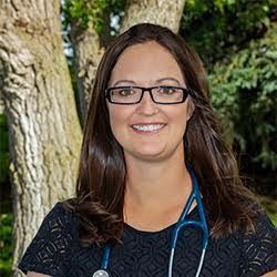 a woman wearing glasses and a stethoscope is smiling in front of a tree .