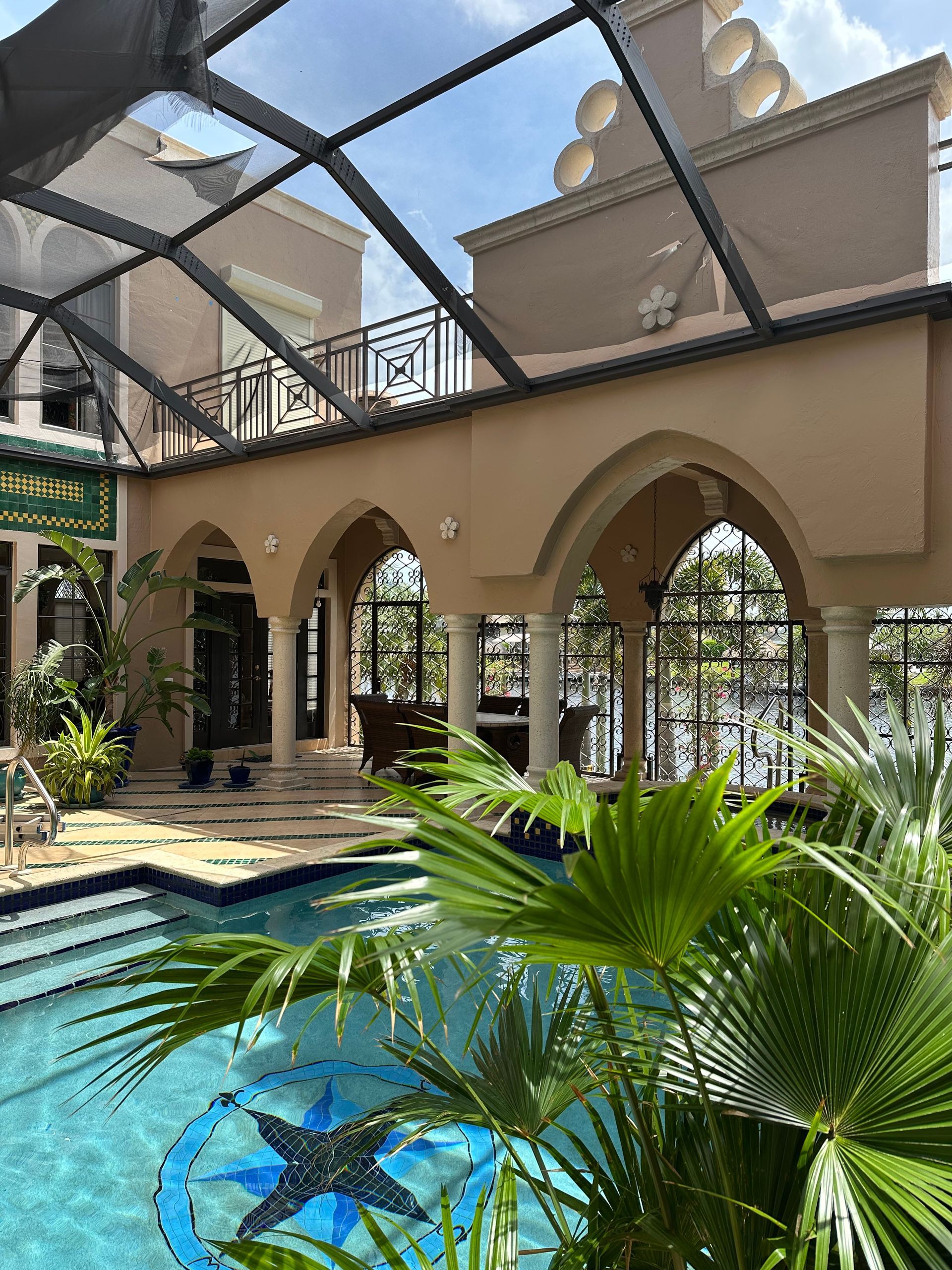 A large swimming pool is surrounded by palm trees and a building.