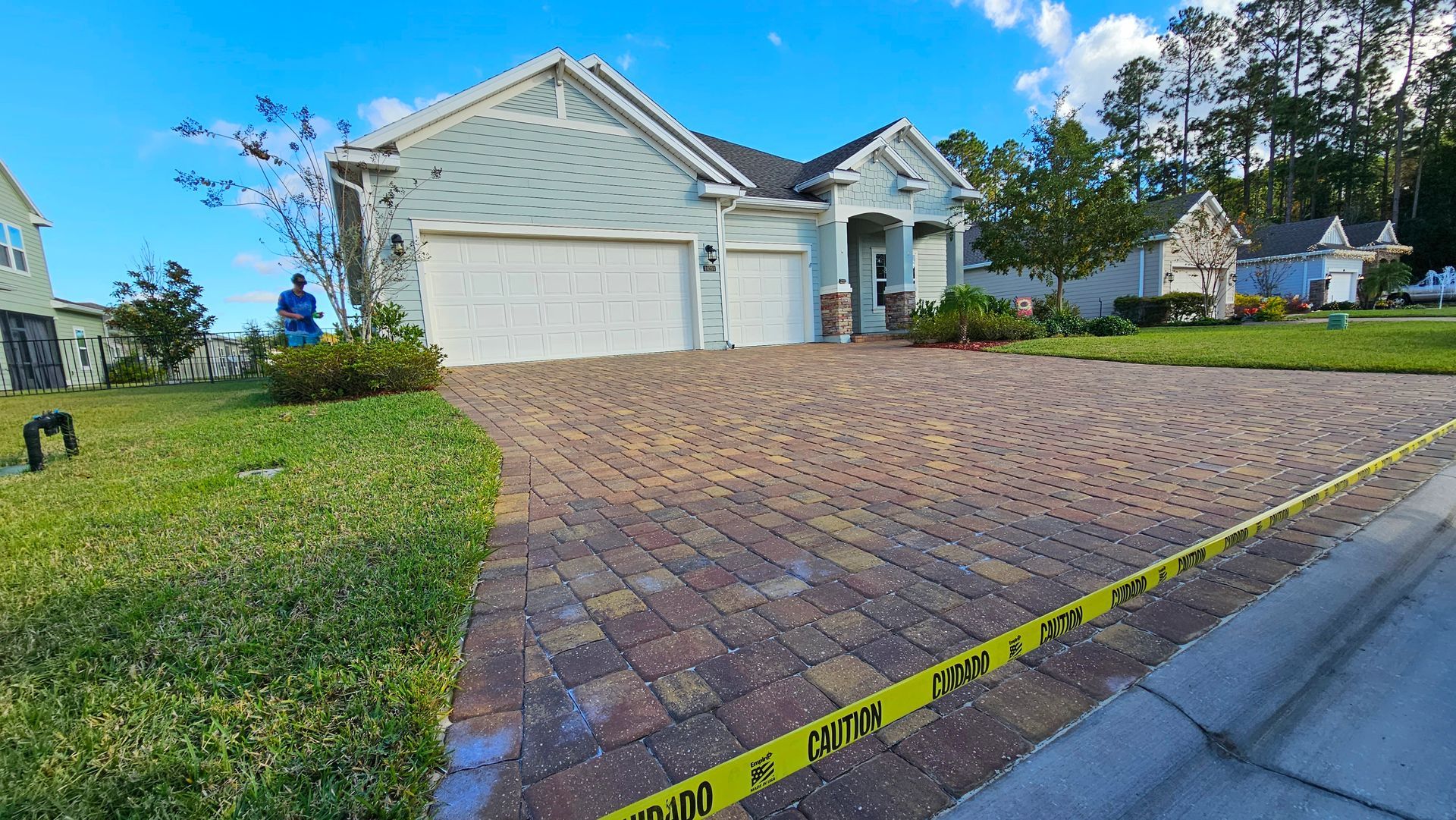 Suburban house with brick driveway, grass, and caution tape on the side of the road.