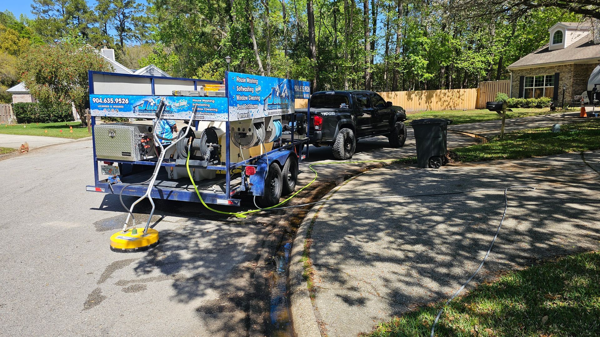 Blue power washing trailer next to black truck parked on a driveway, spraying the curb.