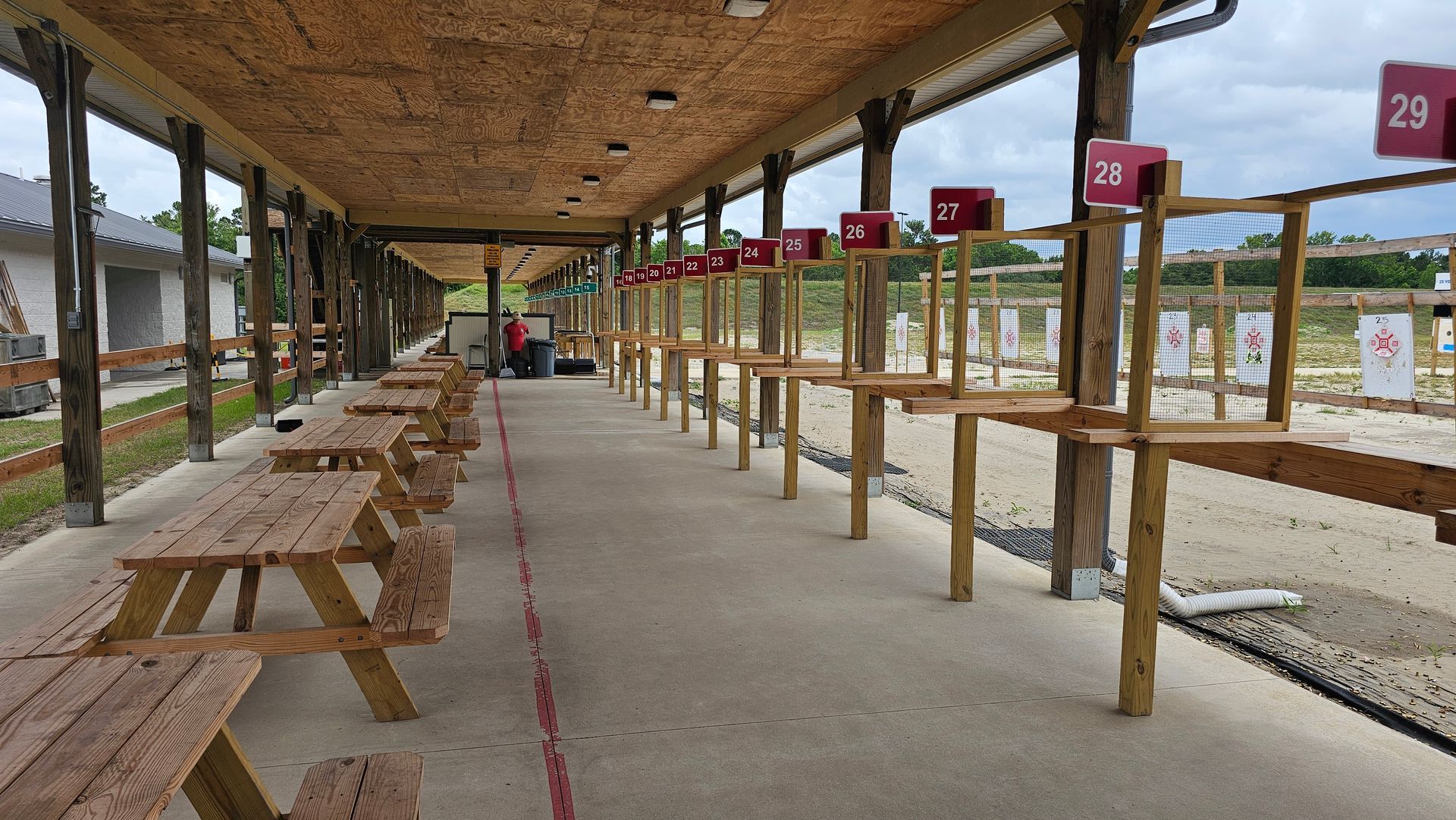 Shooting range with wooden tables and booths. Numbered target posts. Covered concrete pathway.