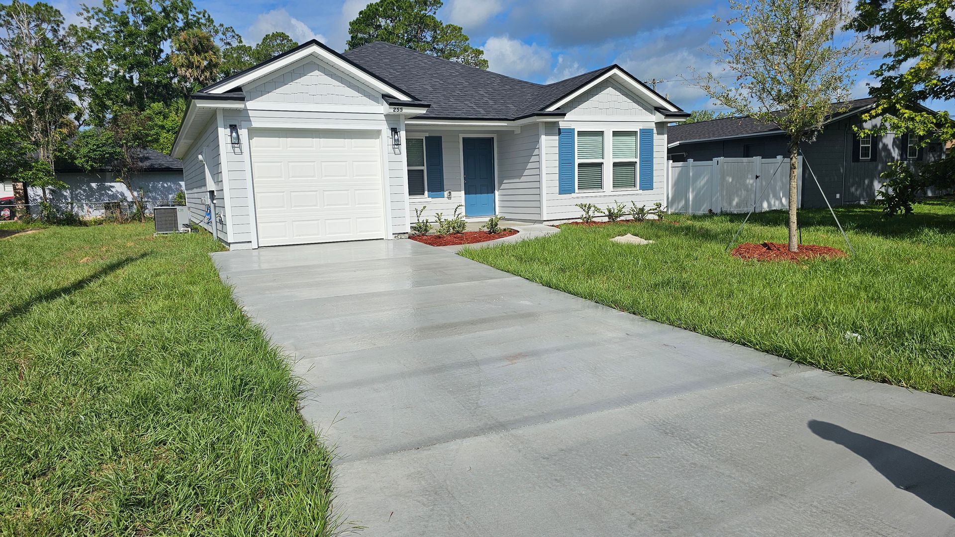 White house with blue door and shutters, gray driveway, green lawn, blue sky.