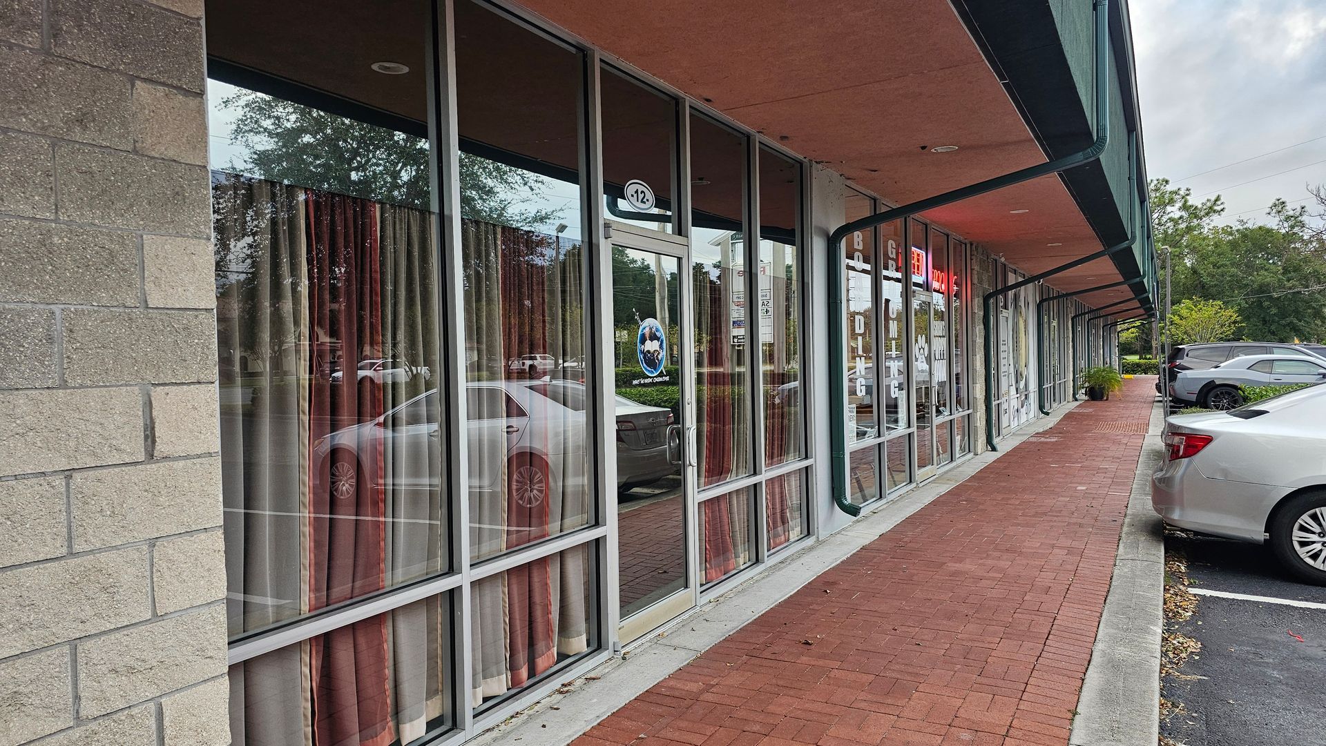 Storefront with large windows, red brick walkway, and parked cars.
