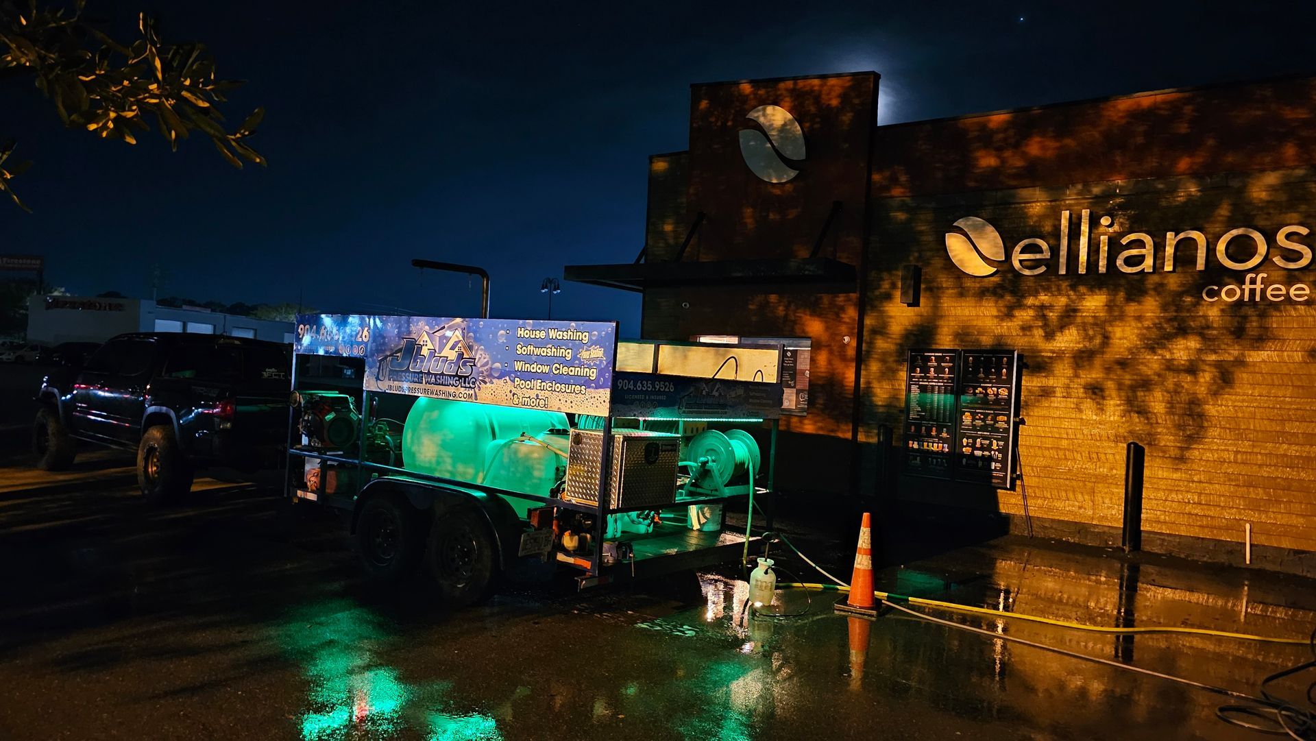 A truck with illuminated water tank parked outside Ellianos Coffee at night, with moon in sky.