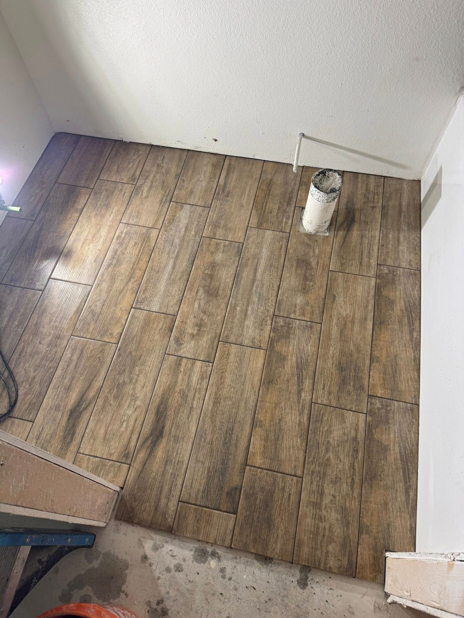 Flooring installation in progress: Wood-look tiles partially covering a room. Brown tones, ceiling in background.