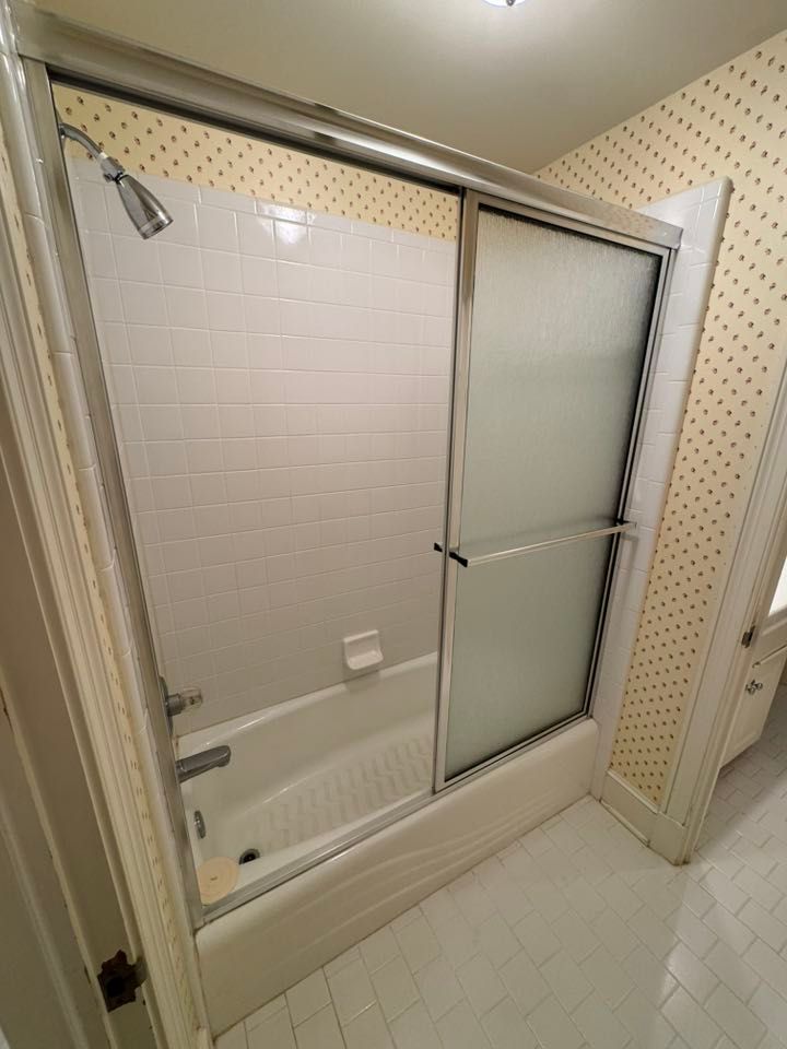 White tiled shower with sliding glass doors in a bathroom.  Tub with shower head and soap dish visible.