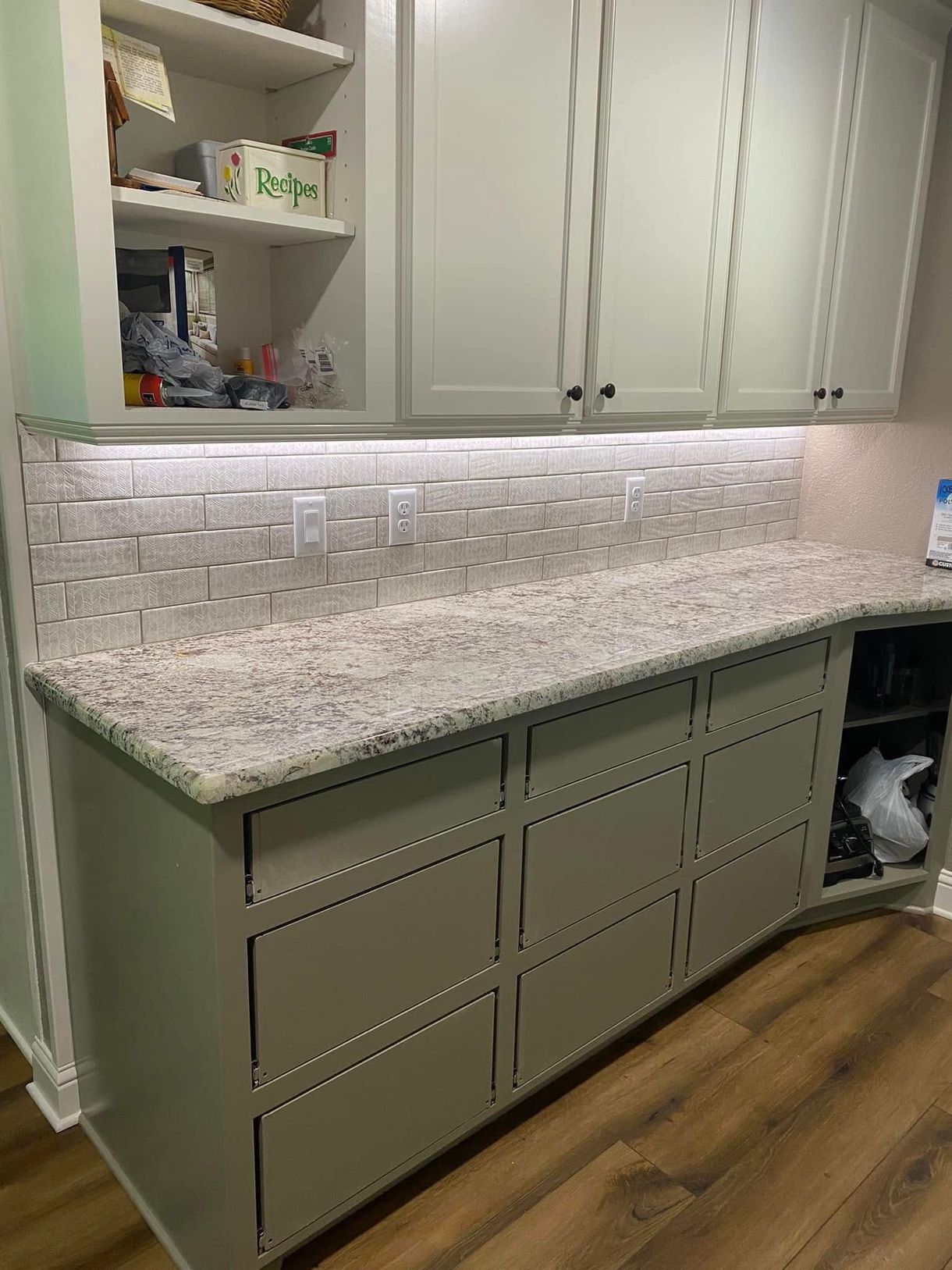 Kitchen with light gray cabinets, white countertop, backsplash, and wooden floor.