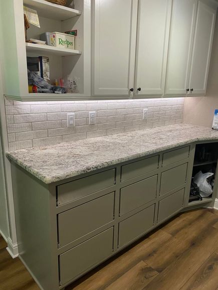 Kitchen with light gray cabinets, white countertop, backsplash, and wooden floor.