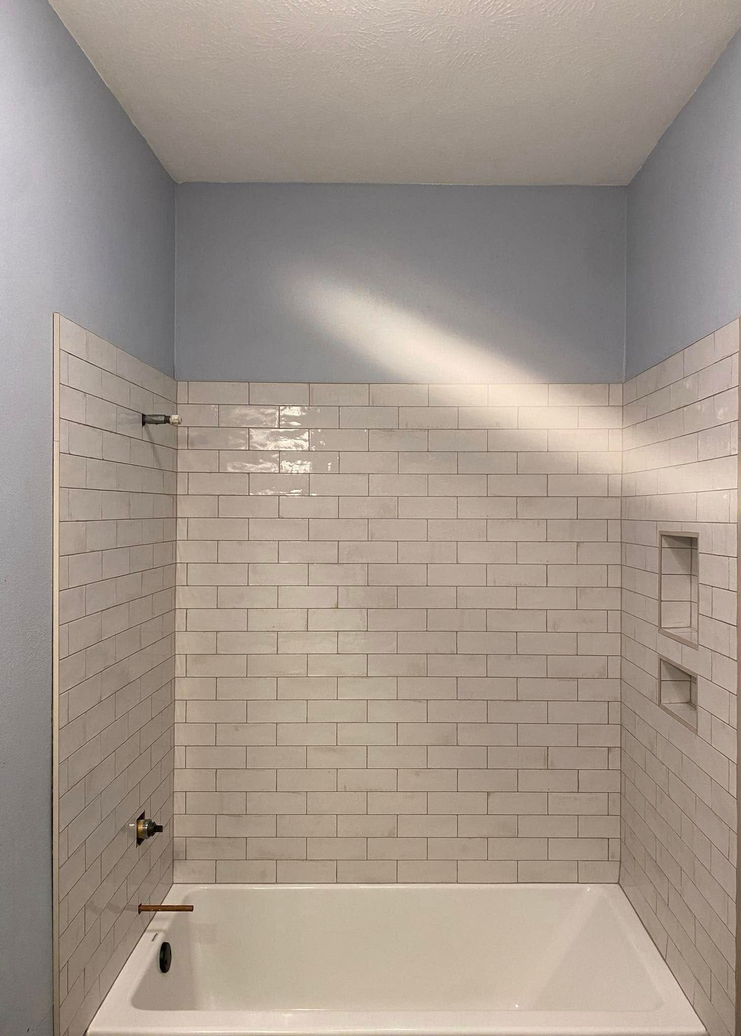 White-tiled shower with a built-in shelf, blue walls above the tile, and a white bathtub.