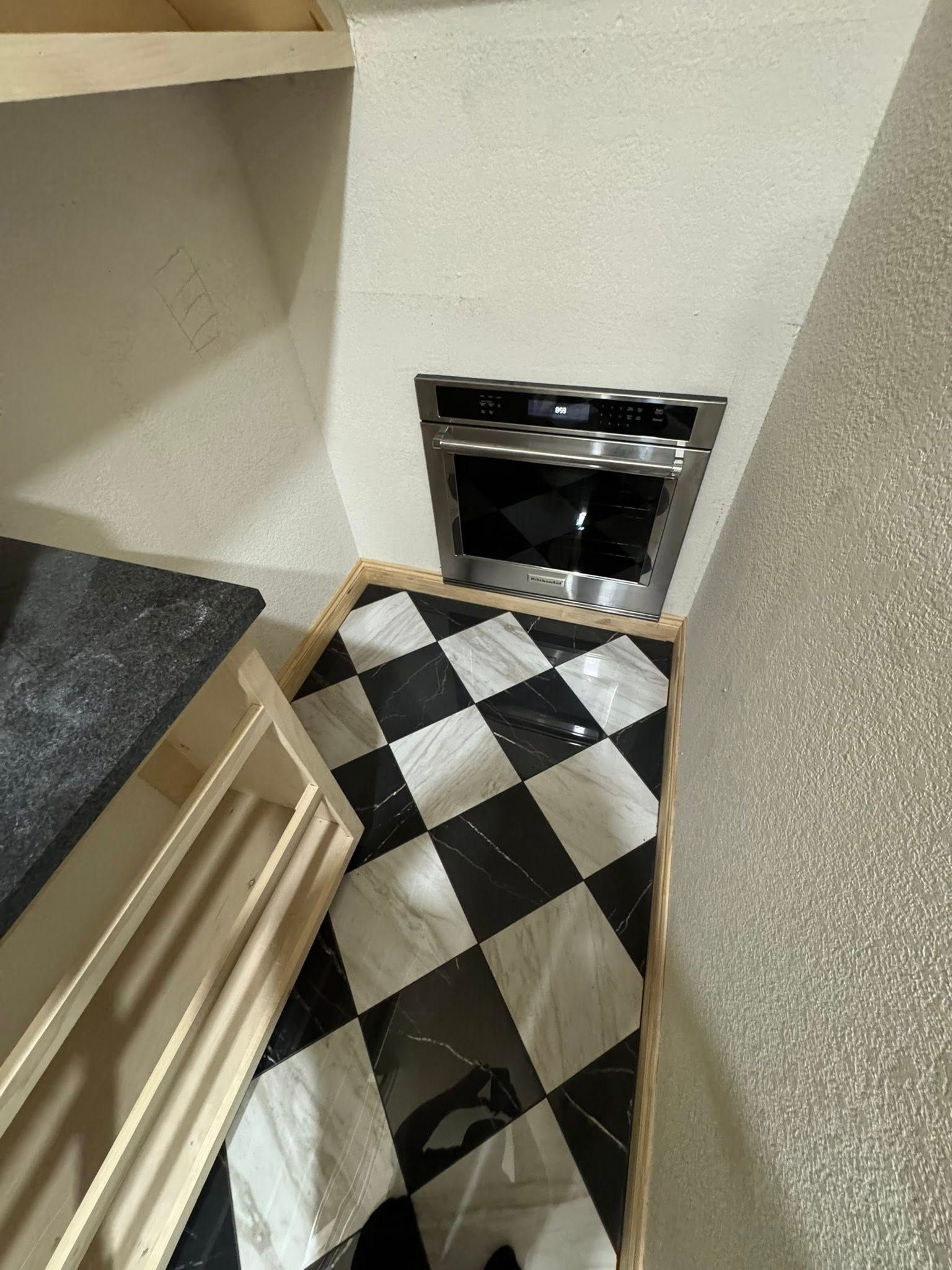 Built-in oven in a kitchen corner with checkered black and white floor tiles.