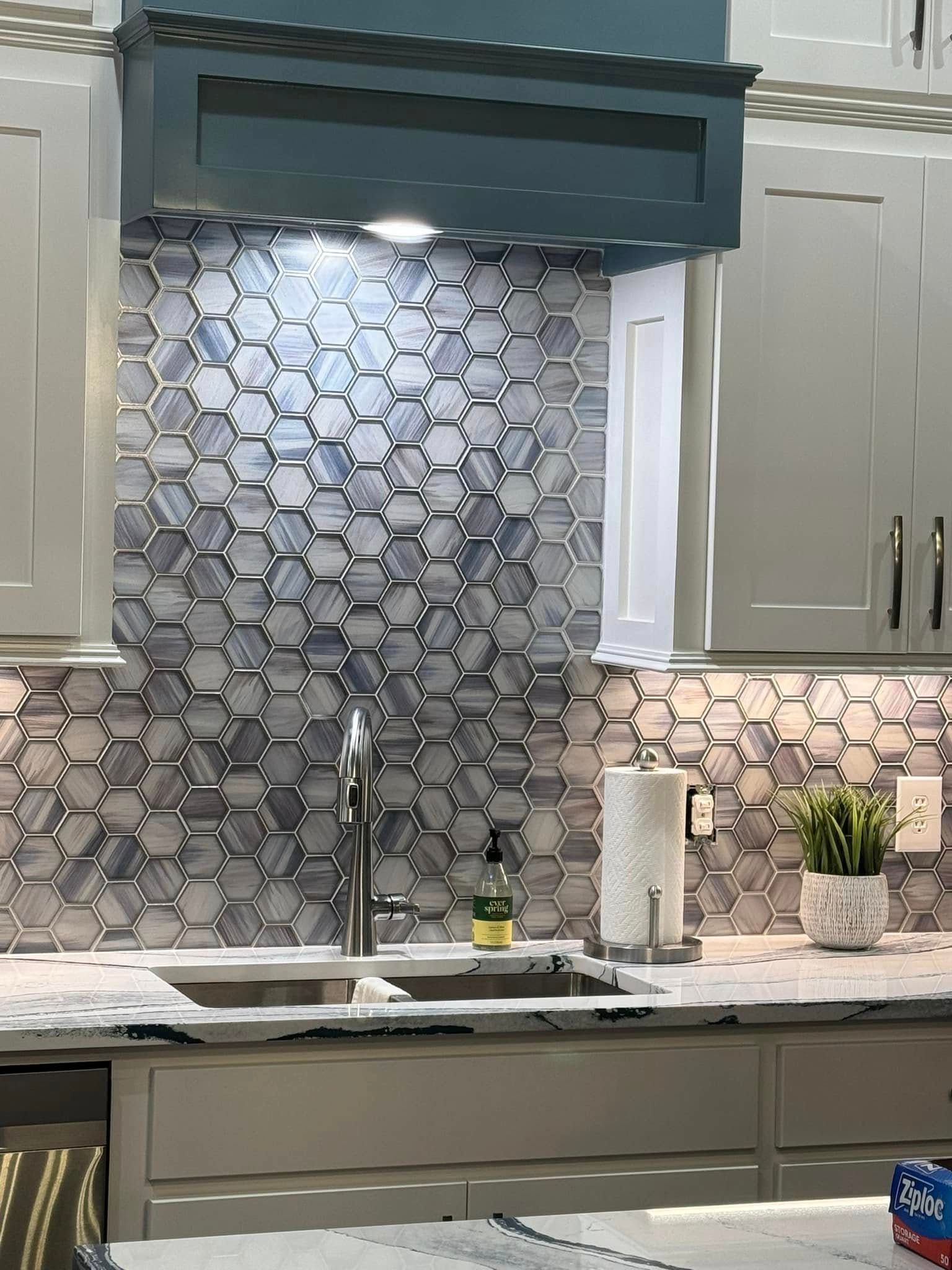 Kitchen with gray cabinets, hexagonal blue and gray tile backsplash, and a stainless steel sink.