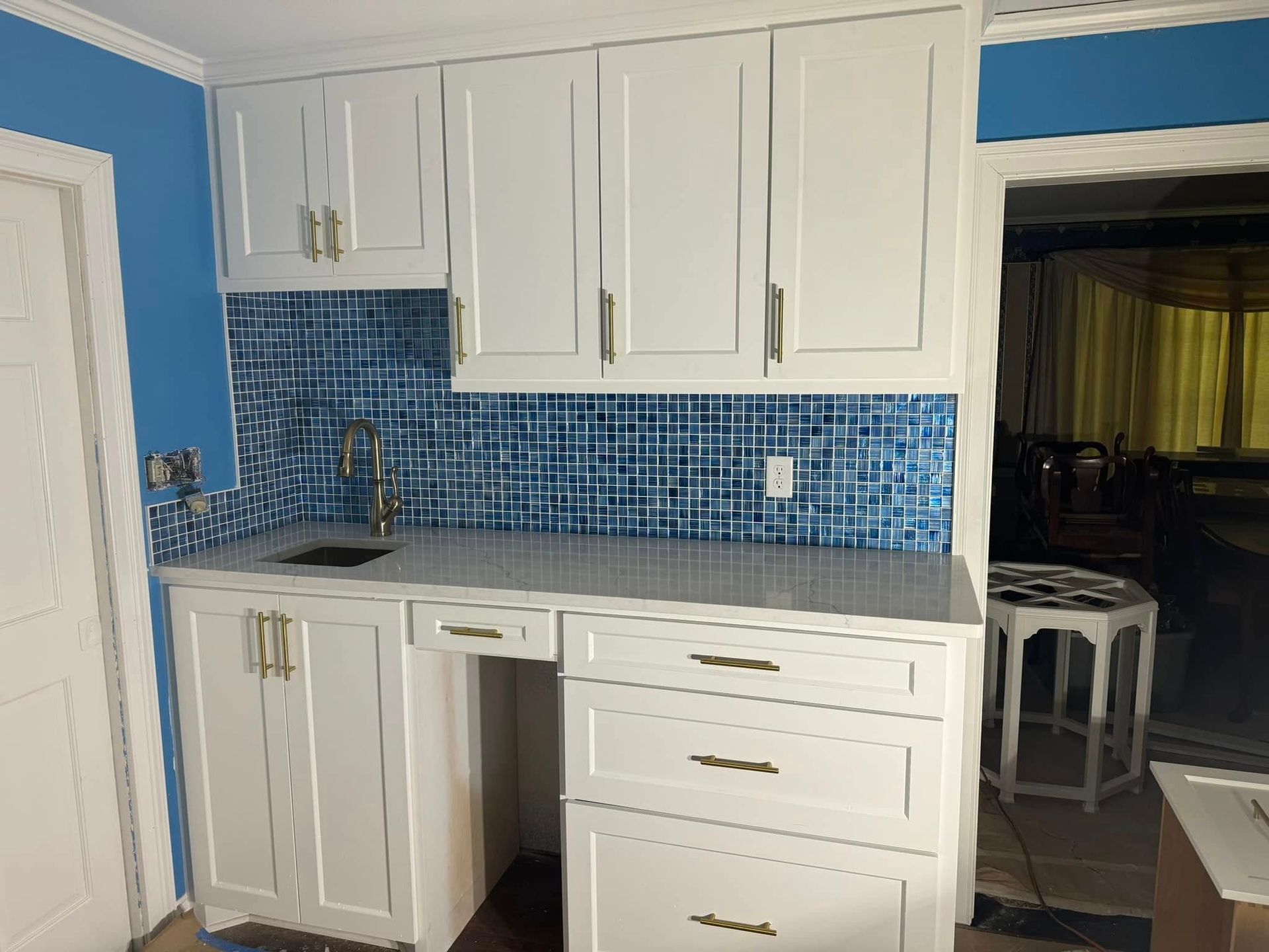 White cabinets with gold handles, blue backsplash, gray countertop, and a small sink.