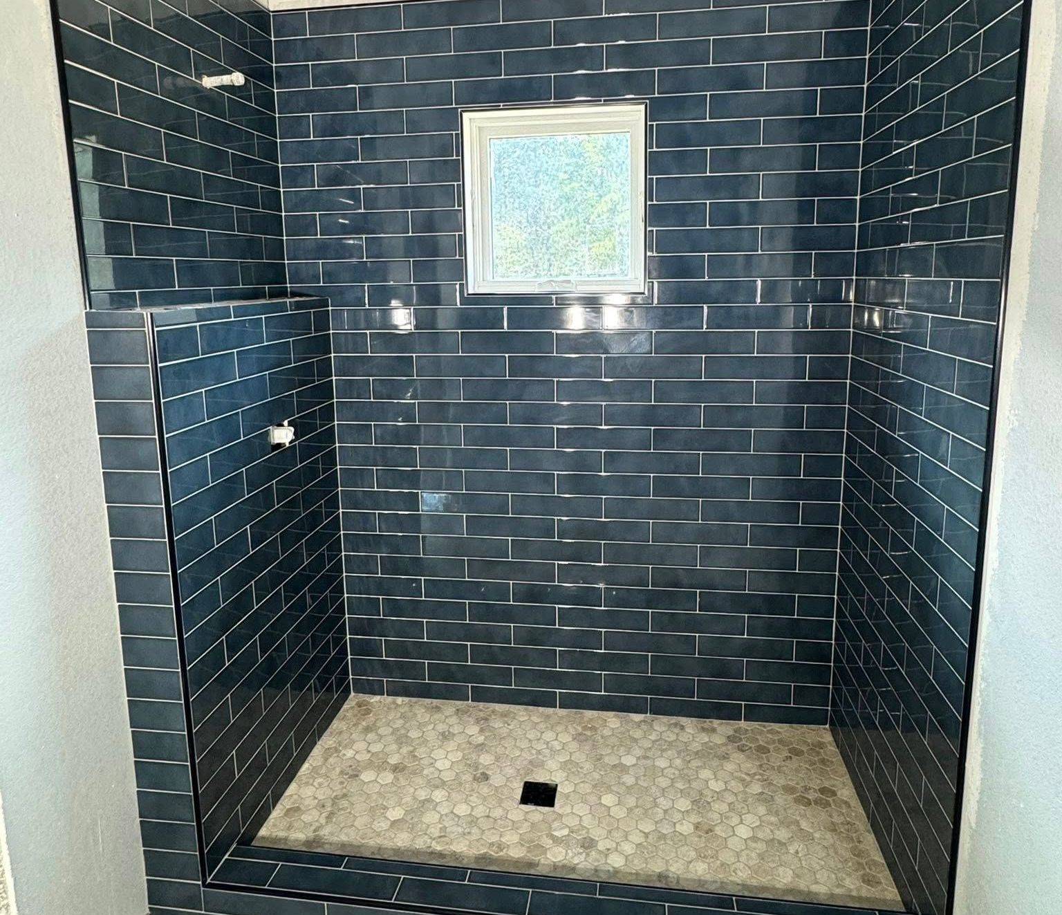 Blue tiled shower with small window, stone floor, and shower heads.