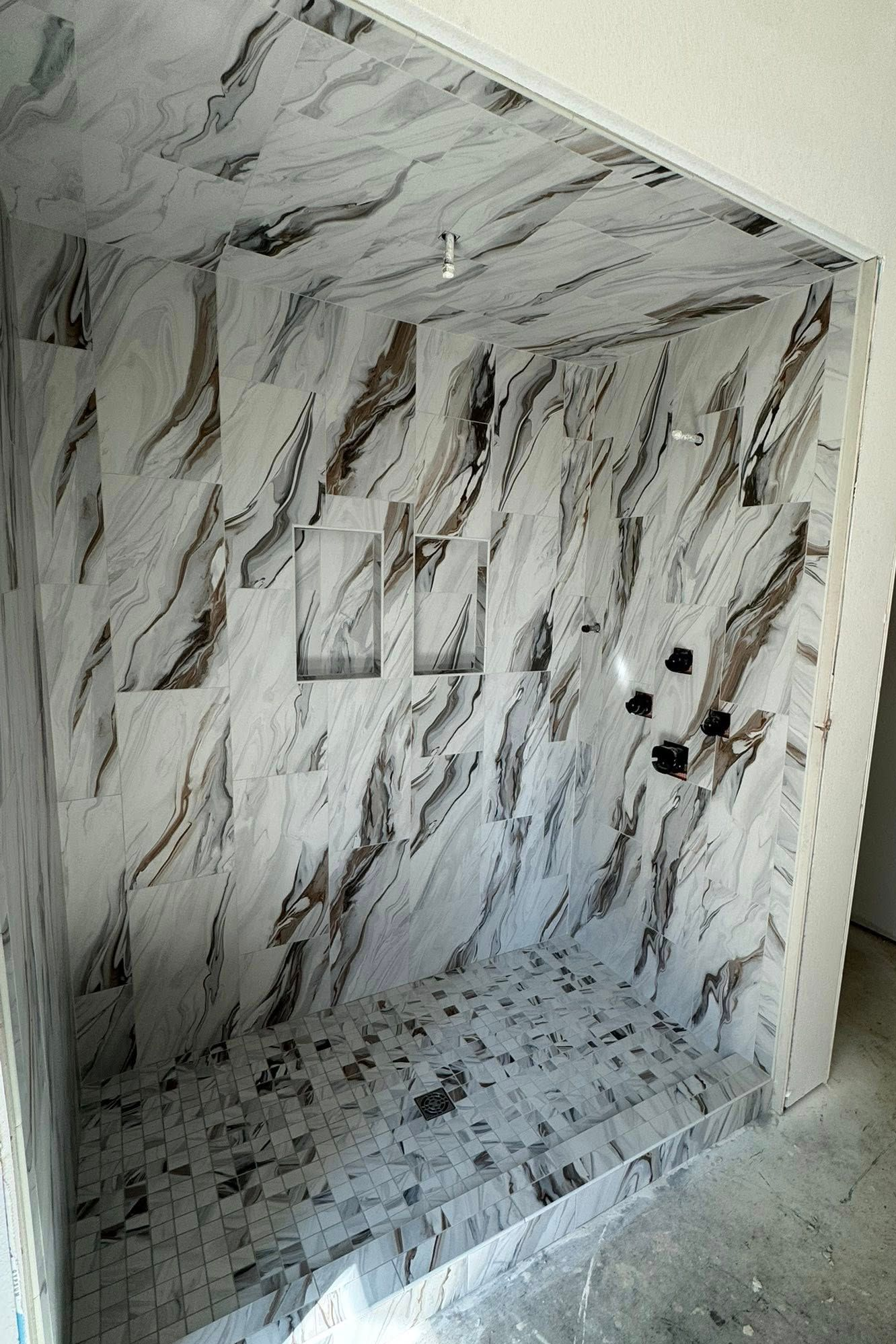 Shower with marble-look tile walls, ceiling, and floor. Three built-in niches and black fixtures.