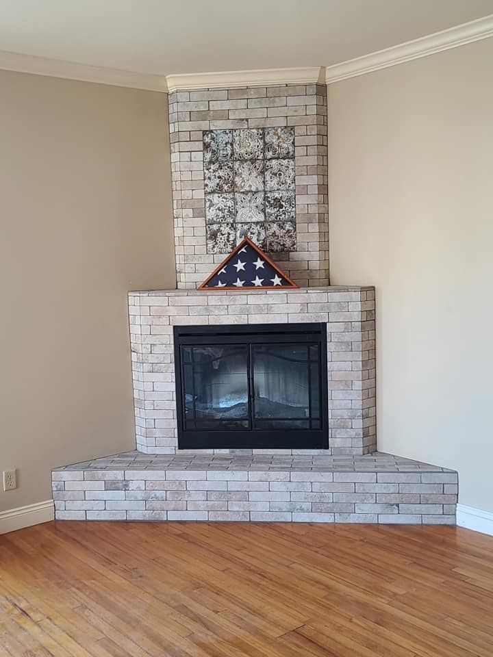 Corner fireplace with gray brick facade, hearth, and mantel, holding a folded American flag.