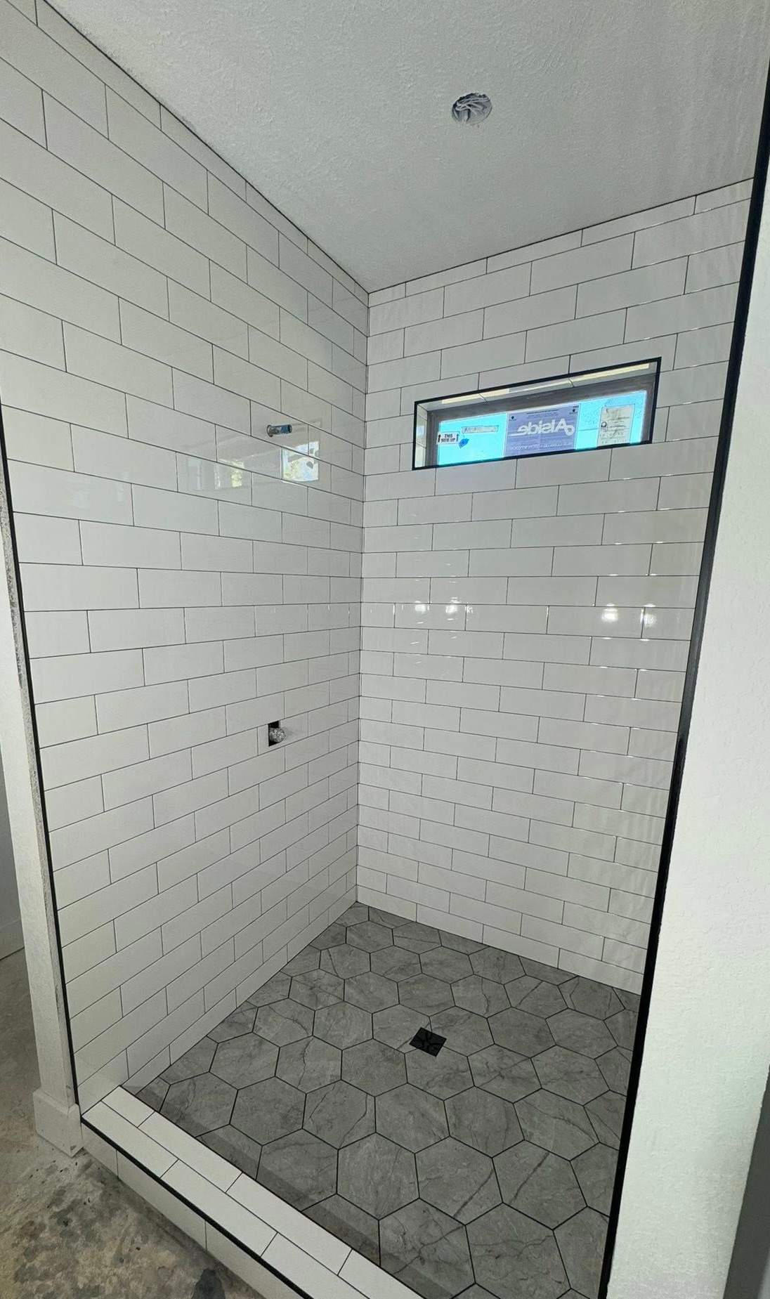 Shower stall with white rectangular wall tiles and hexagon floor tiles; small window.