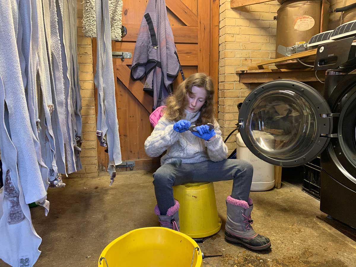 a girl sits on a yellow bucket cleaning horseshoes