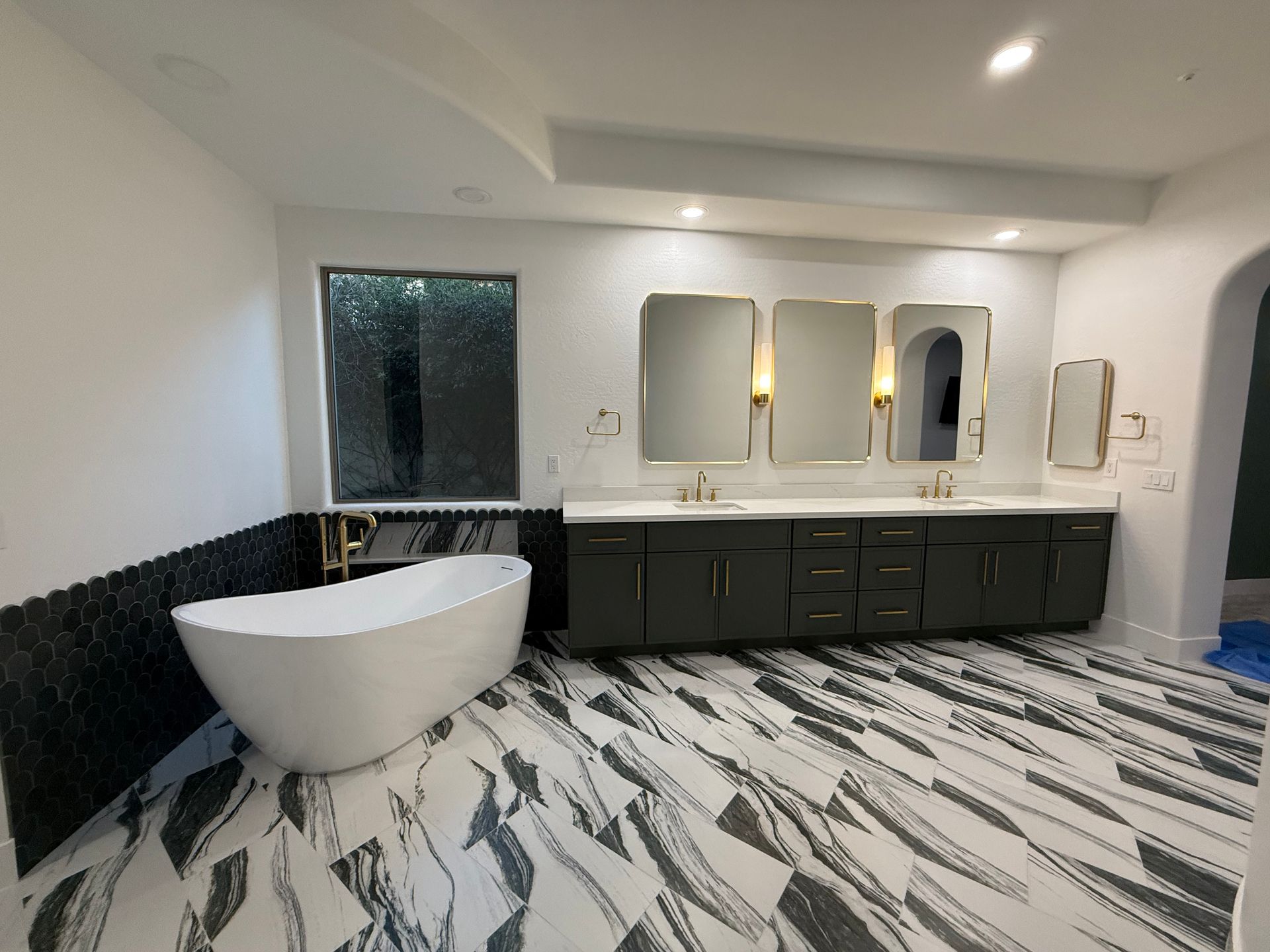 Modern bathroom with black vanity, round tub, mirrors, and black-and-white patterned floor tiles