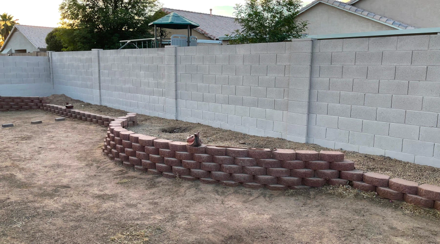 A brick wall is being built in a backyard next to a house.