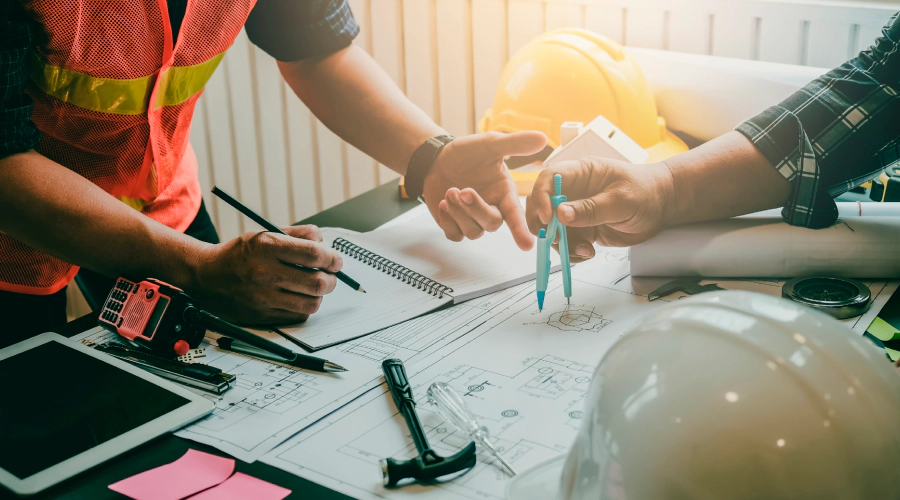 Two construction workers are sitting at a table looking at a blueprint.