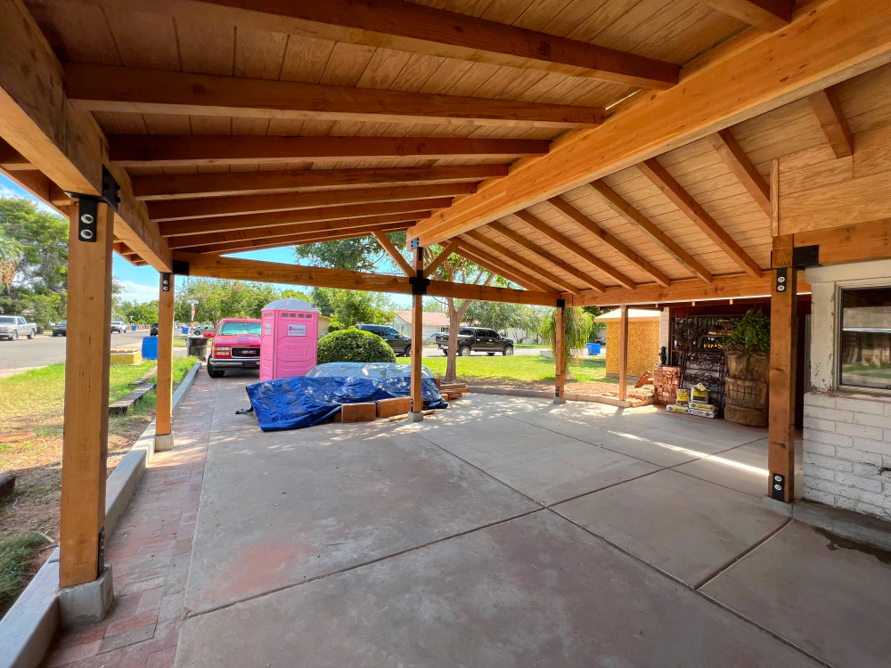 A car is parked under a wooden covered driveway.