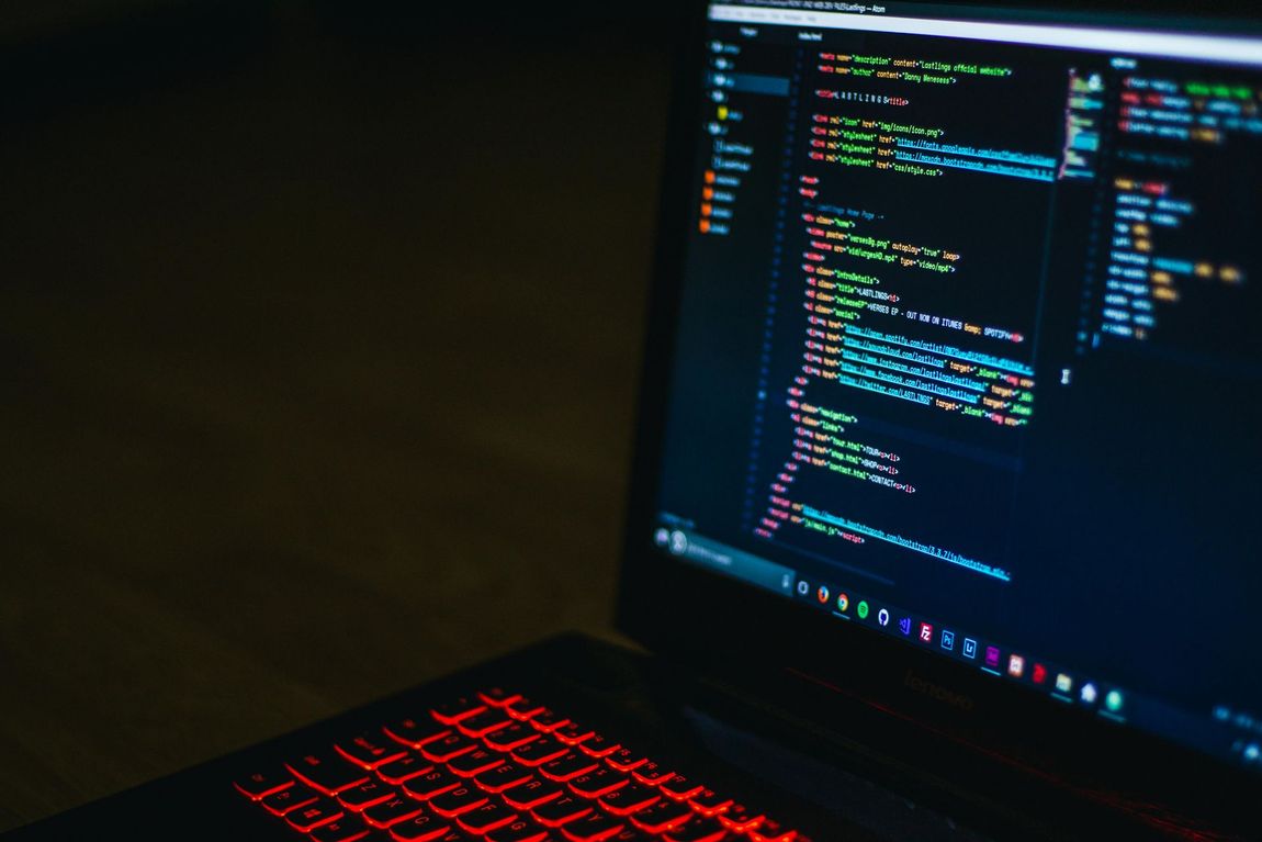 Écran d'ordinateur portable affichant un code coloré, rétroéclairage du clavier rouge dans une pièce sombre.
