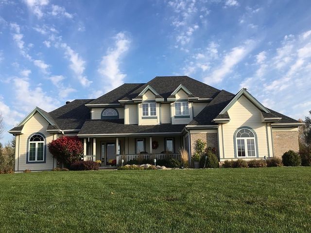 A large house with a black roof is sitting on top of a lush green field.