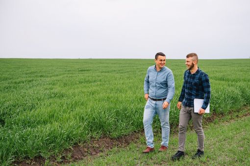 Two people in casual clothing walk through a vibrant green field, smiling and talking while holding a clipboard.