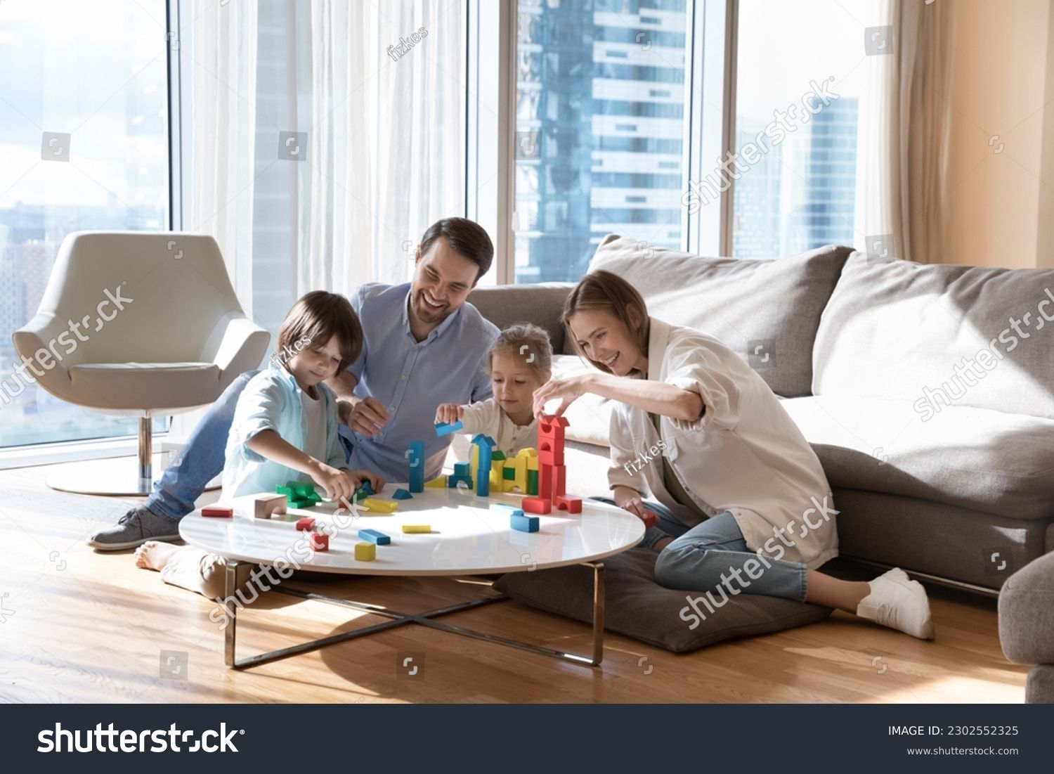 Family playing with colorful building blocks on a round coffee table in a bright, modern living room.