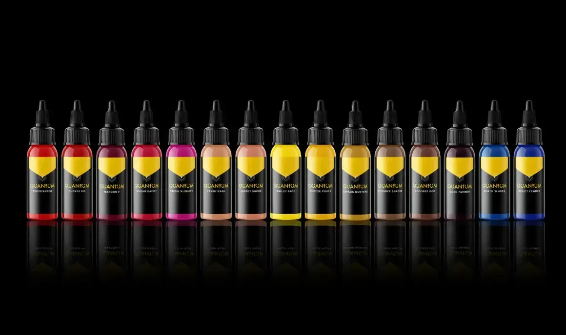 Row of tattoo ink bottles in various shades of yellow, red, and blue against a black background.