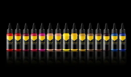 Row of tattoo ink bottles in various shades of yellow, red, and blue against a black background.