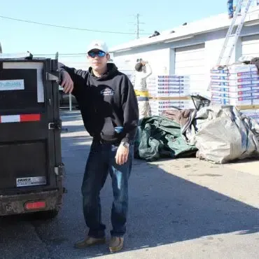 A man is leaning against a dumpster with a sticker on it that says hydraulics