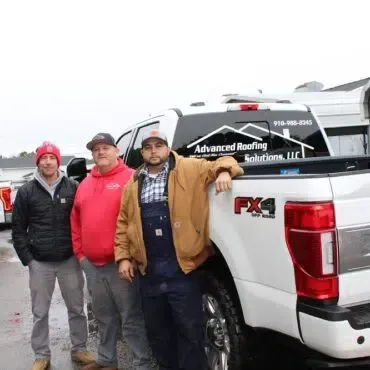 A group of men are standing next to a white truck.