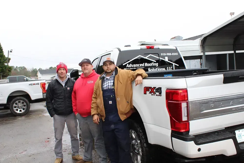 Three men are standing next to a white truck in a parking lot.