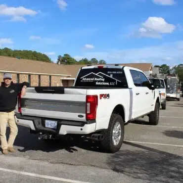 A man is standing next to a white truck in a parking lot.