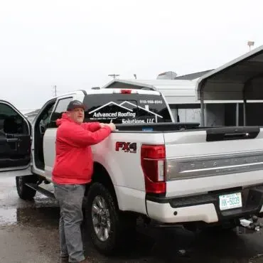 A man in a red jacket is standing next to a white truck.