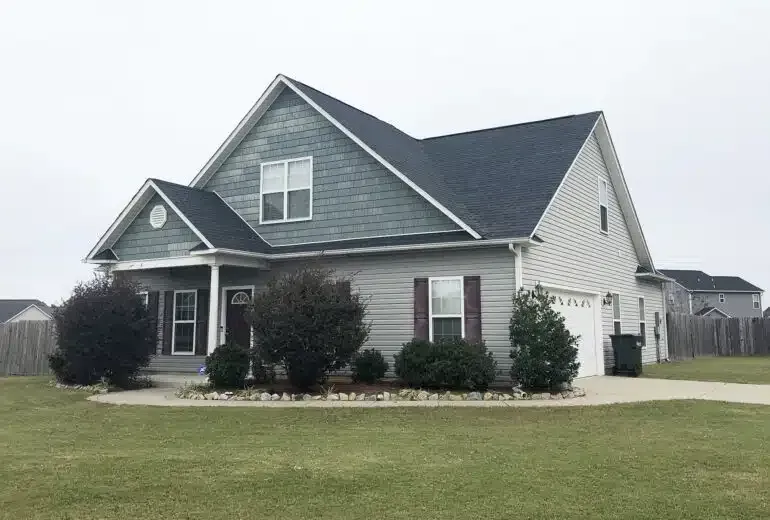 A large house with a blue siding and a black roof is sitting on top of a lush green field.