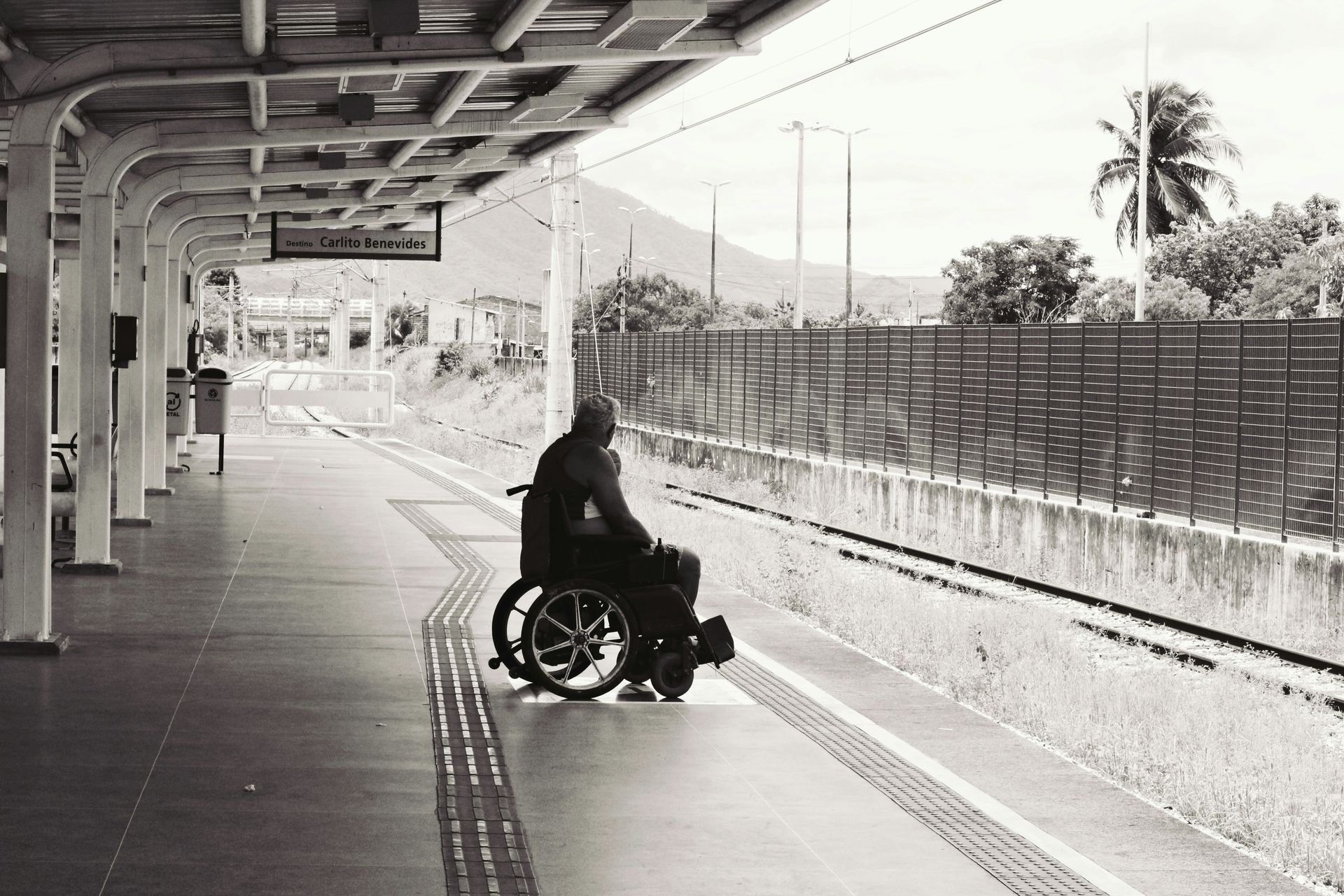 Man in a wheelchair looking into the distance while waiting alone on a train station platform.
